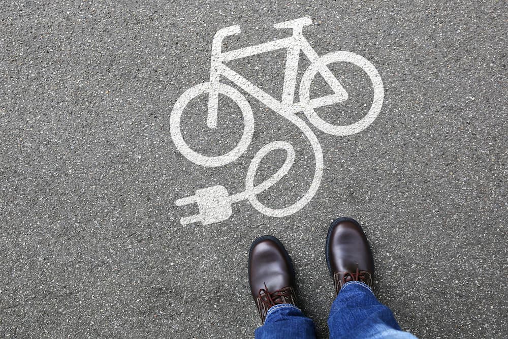 Person standing over electric bike symbol on street.